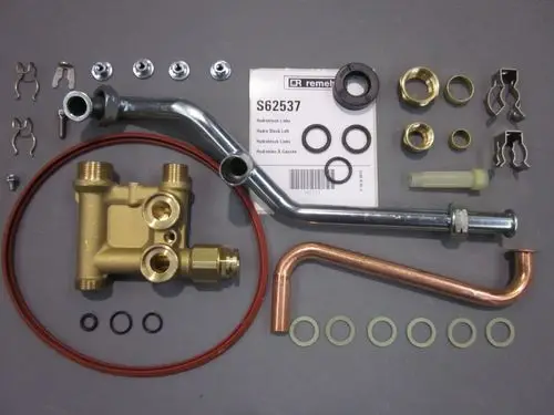 Remeha Hydroblock mit verschiedenen Verbindungselementen, Dichtungen und Schläuchen sowie Montageanleitung. Komponenten angeordnet auf grauem Untergrund.